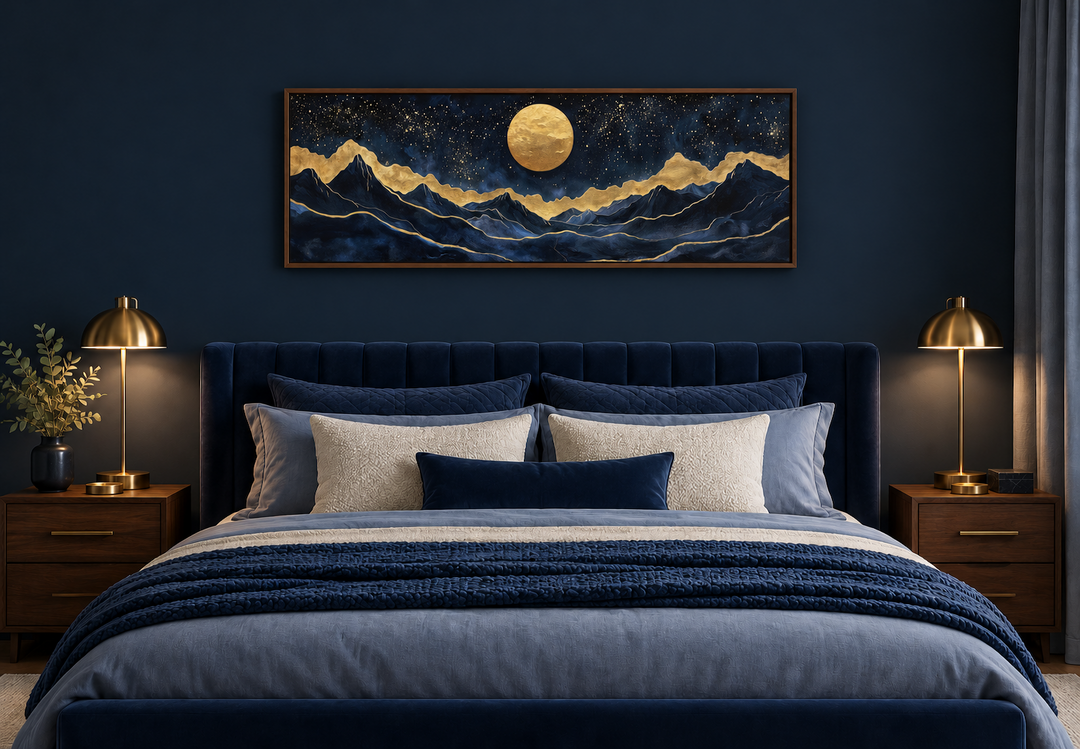 Panoramic canvas print of a gold moon over navy mountains above a bed in a dark blue bedroom.