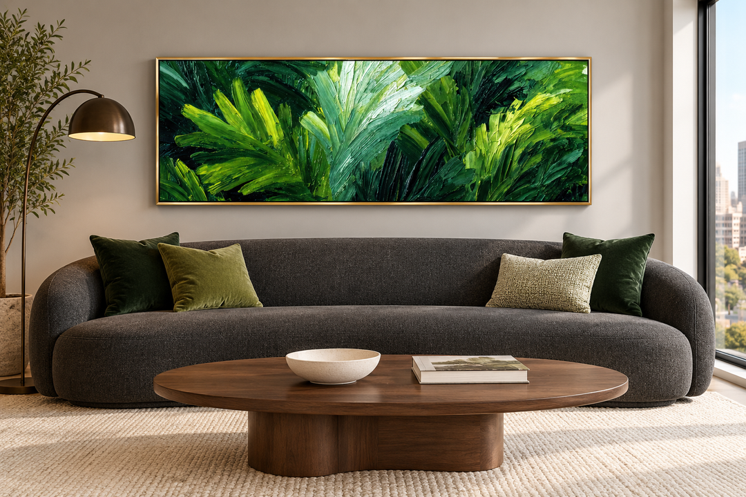 Panoramic rainforest jungle leaves canvas wall art in a gold frame above a modern charcoal sofa.