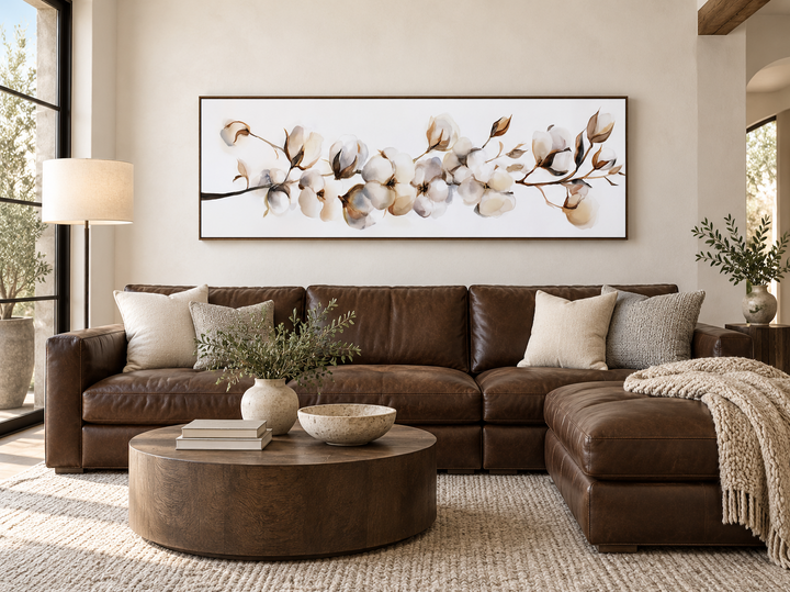 Boho long horizontal neutral cotton plant painting on canvas above a brown leather sectional sofa.