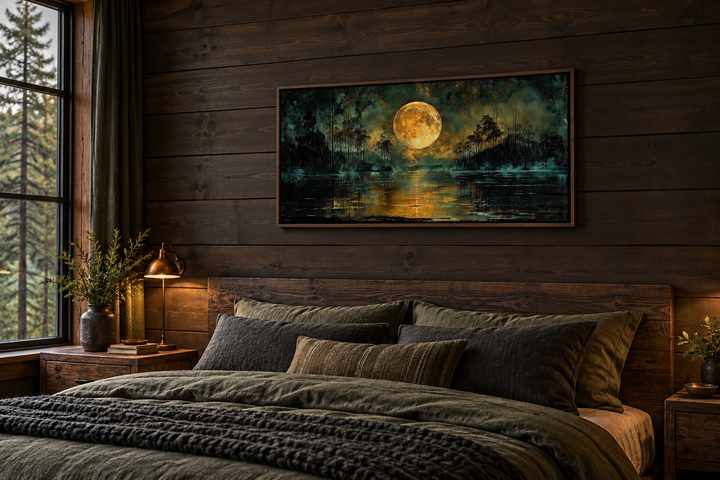 Framed canvas print of a full yellow moon over a dark lake, hanging above a bed in a wooden cabin.