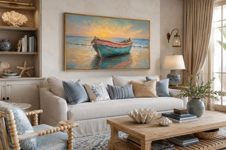 Weathered teal and pink rowboat painting in a gold frame above a sofa in a coastal living room.