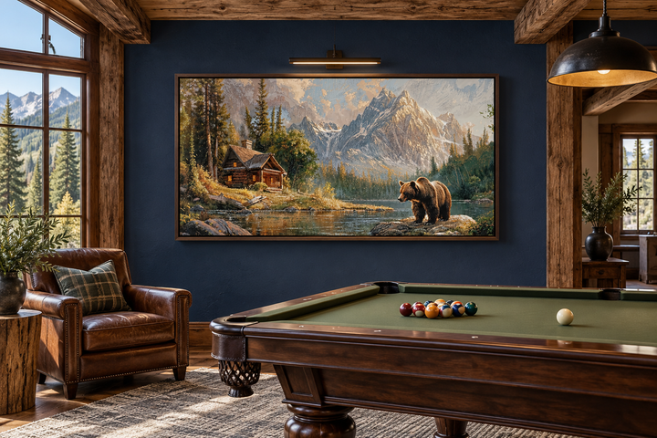 Framed panoramic canvas art of a bear near a mountain cabin by a lake in a rustic billiards room.