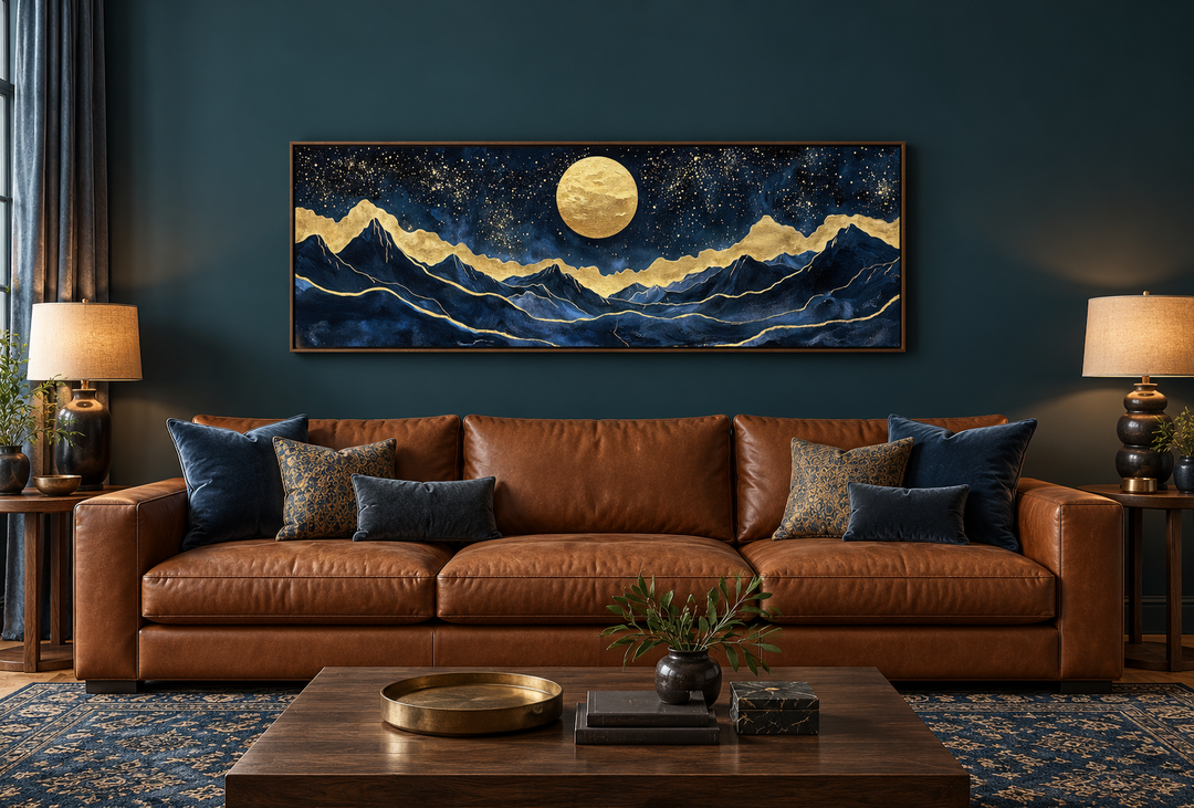Gold and navy moon mountain landscape canvas print above a brown leather sofa in a dark teal room.