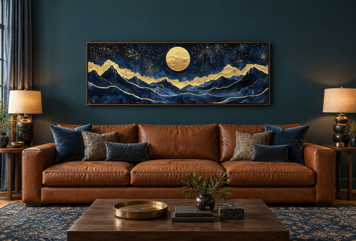 Gold and navy moon mountain landscape canvas print above a brown leather sofa in a dark teal room.