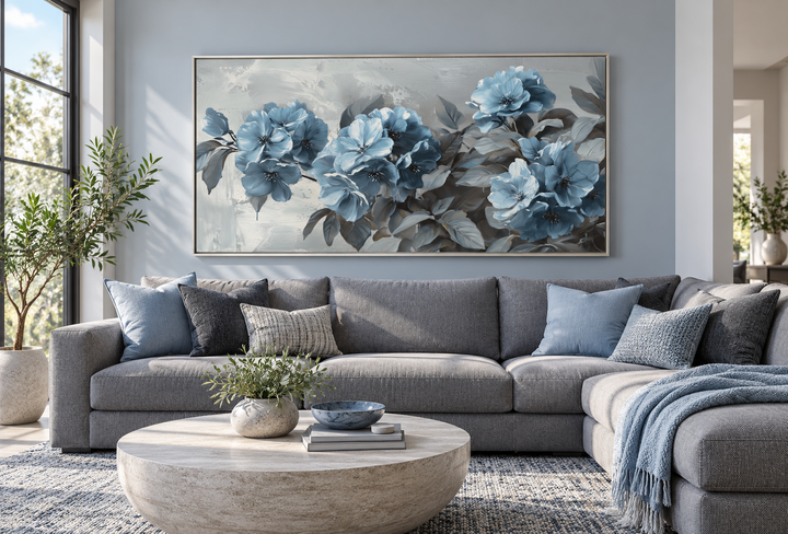Large horizontal canvas print of light blue abstract flowers on a grey background above a sofa.