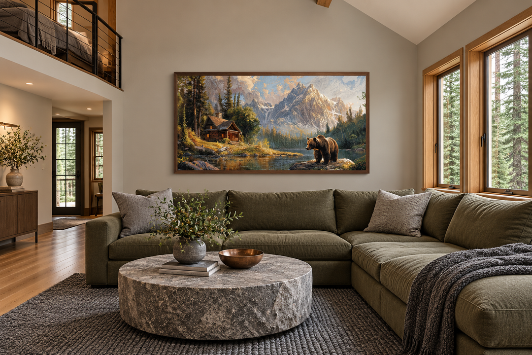 Framed panoramic canvas of a bear near a mountain cabin and lake in a rustic living room.