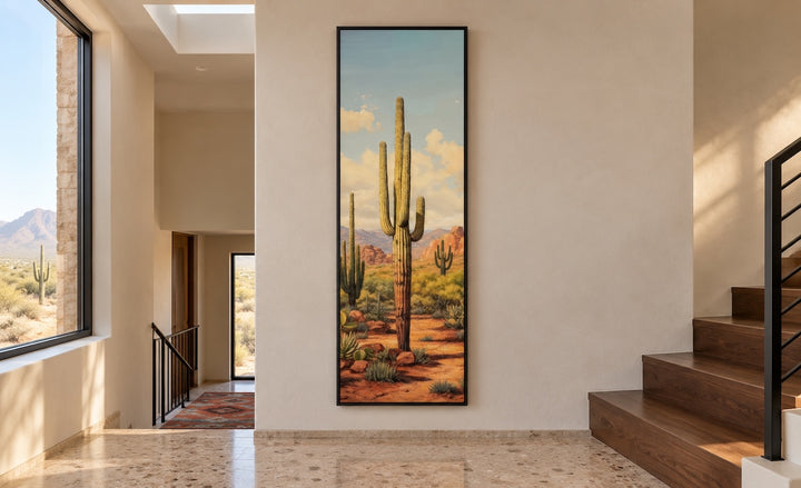Tall vertical saguaro cactus canvas wall art in a black frame on a neutral hallway wall.