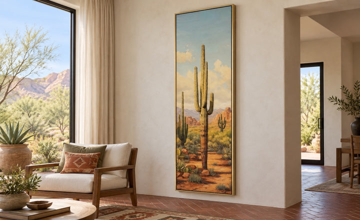Tall vertical saguaro cactus canvas wall art in a gold frame on a neutral wall in a sunroom.