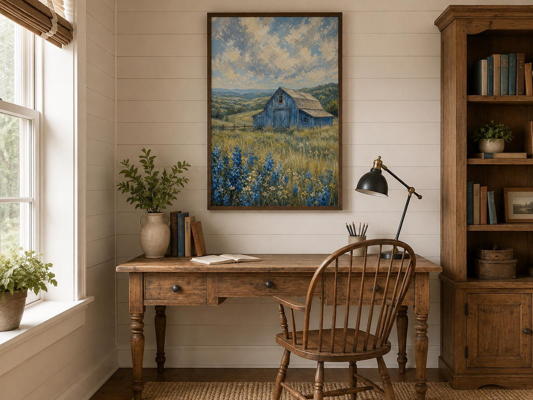 Vertical canvas art of a blue barn in a field of bluebonnets hanging above a rustic wooden desk.