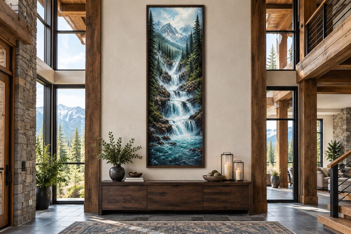 Tall narrow canvas art of a cascading mountain waterfall through a pine forest with snowy peaks.