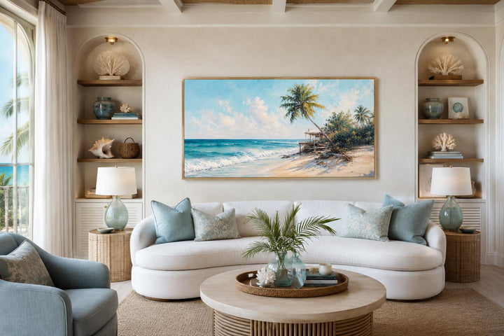 Tropical beach wall art with palm trees and turquoise waves above a white sofa in a coastal room.