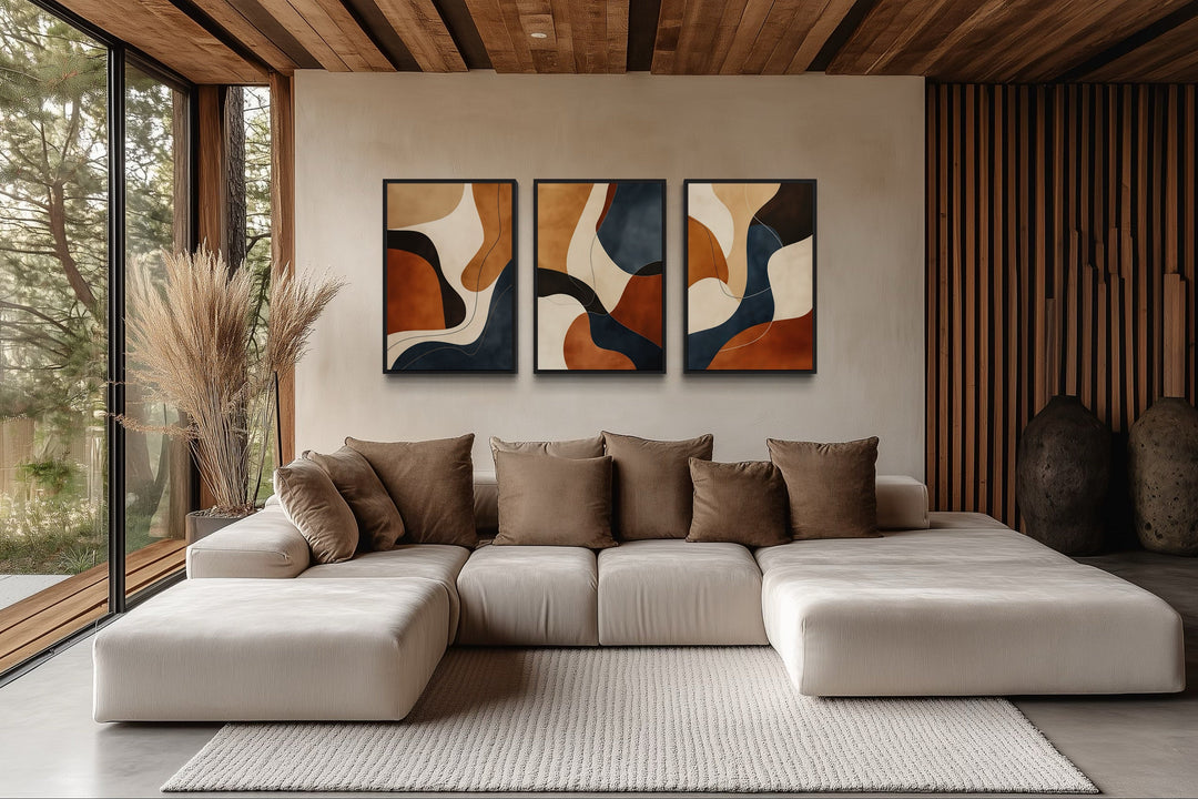 Three-piece mid-century modern abstract wall art in earth tones, cream, and navy above a sofa.