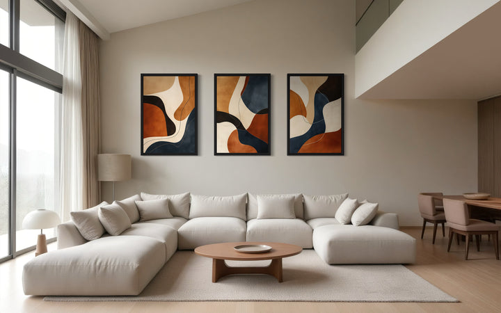 3 piece mid-century modern abstract wall art in earth tones, cream, and navy above a beige sofa.