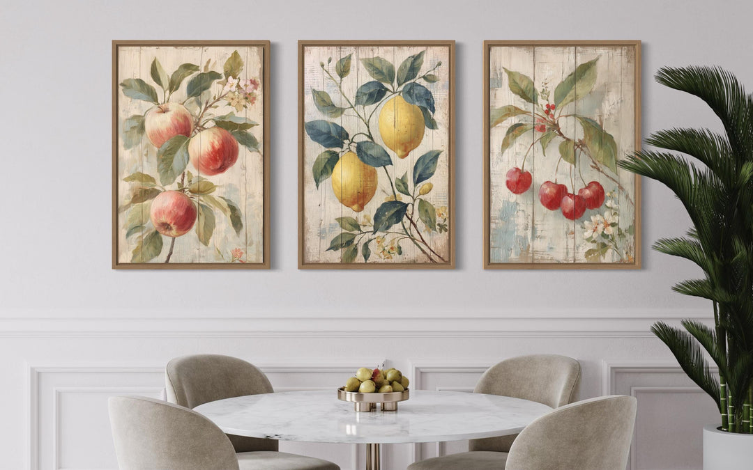Three rustic framed wall art prints of apples, lemons, and cherries above a marble dining table.