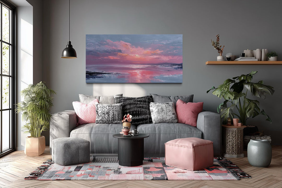 Horizontal canvas wall art of a blush pink ocean sunset hanging above a grey sofa in a living room.
