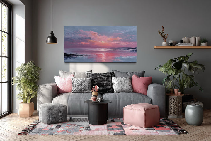 Horizontal canvas wall art of a blush pink ocean sunset hanging above a grey sofa in a living room.