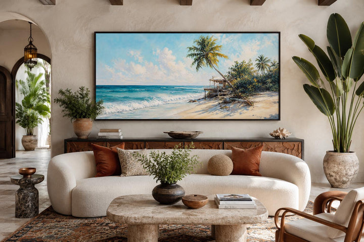 Tropical beach wall art with palm trees and turquoise waves above a sofa in a coastal living room.