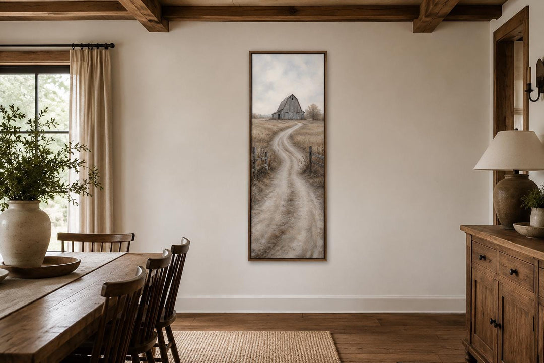 Tall narrow farmhouse wall art of a weathered barn and winding dirt road in a dining room.
