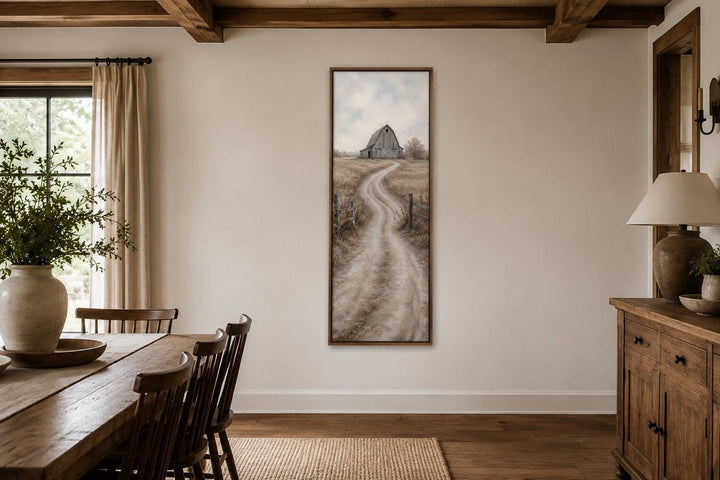 Tall narrow farmhouse wall art of a weathered barn and winding dirt road in a dining room.