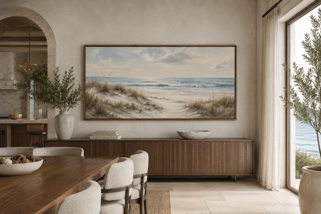 Sandy beach dunes wall art with sea grass and rolling waves in a slim gold frame above a sideboard.