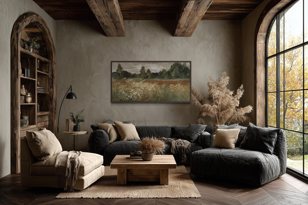 A framed canvas print of a neutral wildflower meadow landscape hangs in a rustic farmhouse room.