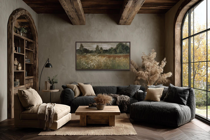 A framed canvas print of a neutral wildflower meadow landscape hangs in a rustic farmhouse room.