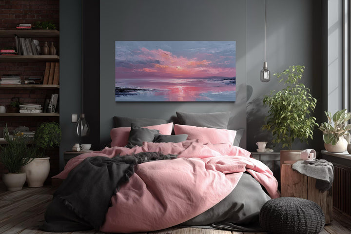 A horizontal canvas print of a pink ocean sunset hangs above a bed with pink and grey linens.