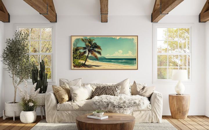 a cozy living room with a large window overlooking a beach, a painting of a palm tree on the wall, and a comfortable couch with pillows and a throw blanket.