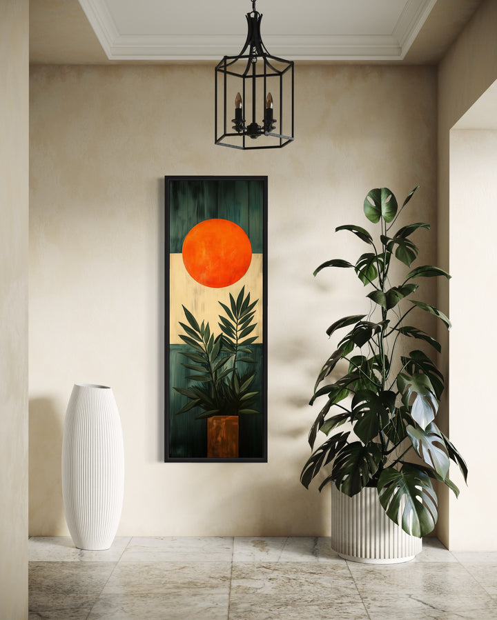 Mid Century Modern Orange Sun And Palm Leaves Framed Canvas Wall Art next to a potted plant