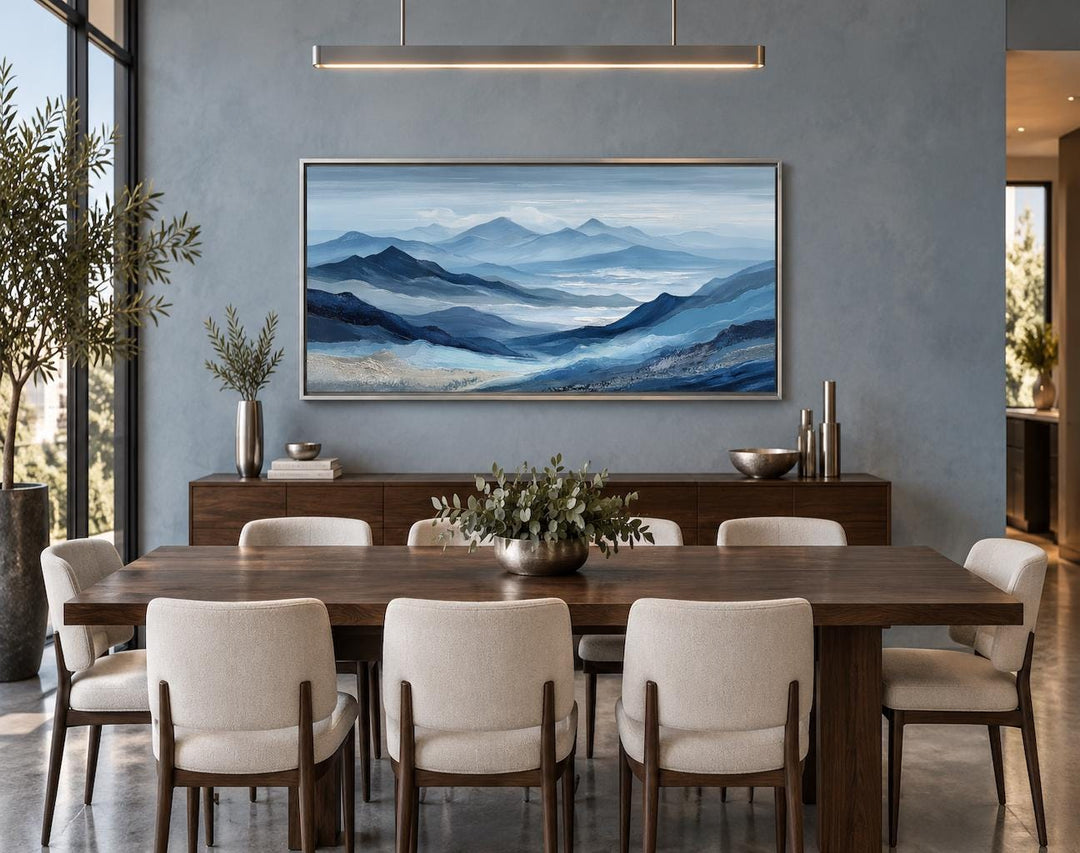 Blue mountain landscape canvas wall art in a silver frame above a dark wood dining table.