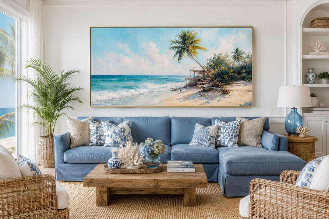 Tropical beach wall art with palm trees and turquoise waves above a blue sofa in a coastal room.