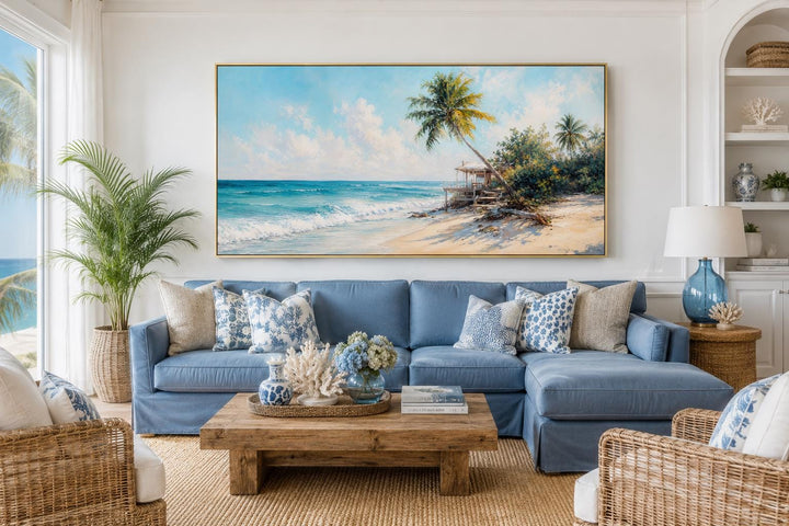 Tropical beach wall art with palm trees and turquoise waves above a blue sofa in a coastal room.
