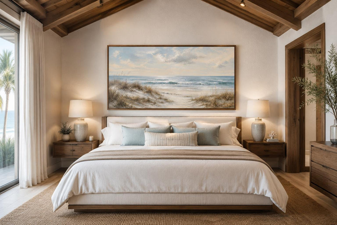Sandy beach dunes wall art with sea grass and rolling waves in a slim gold frame above a bed.