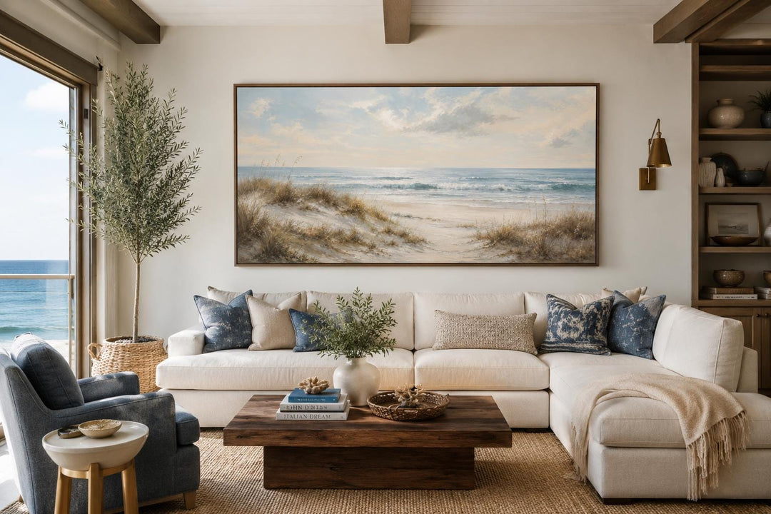Sandy beach dunes wall art with sea grass and rolling waves in a slim gold frame above a sofa.
