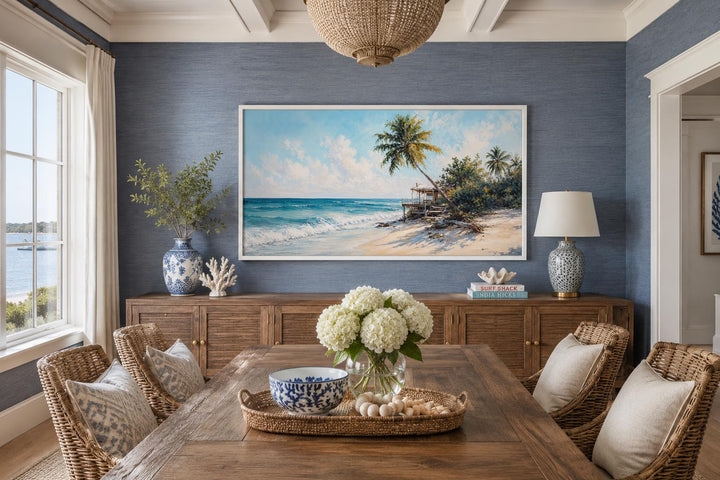 Tropical beach painting with palm trees and turquoise waves in a white frame on a blue wall.