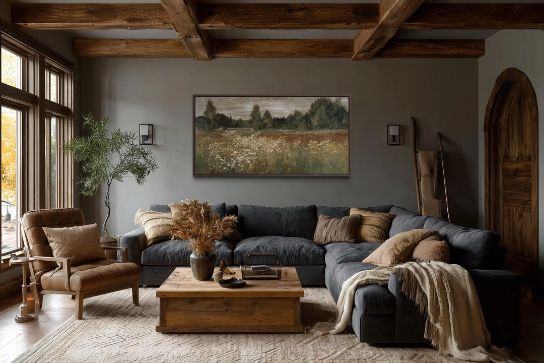 A framed canvas print of a neutral wildflower meadow landscape hangs in a rustic farmhouse room.