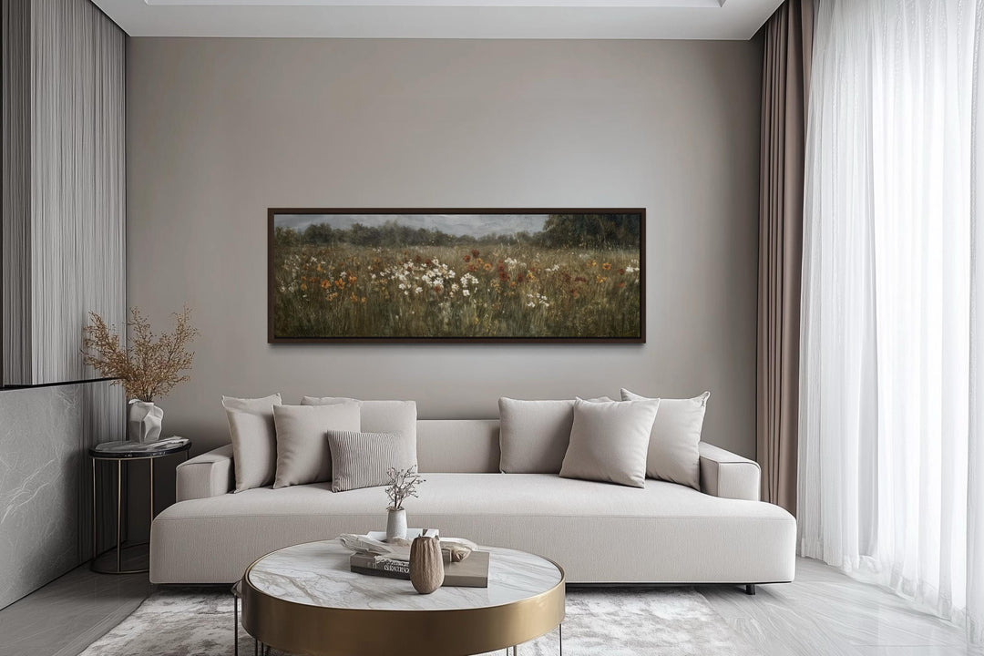 A long horizontal canvas of a moody wildflower field hangs above a modern sofa in a neutral room.