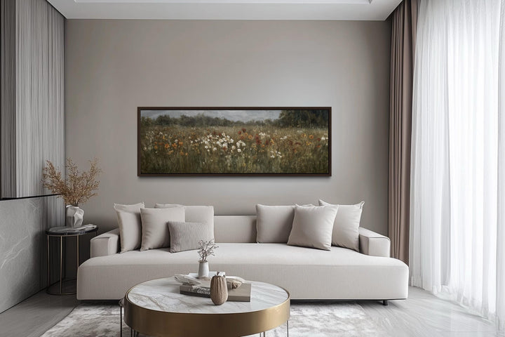 A long horizontal canvas of a moody wildflower field hangs above a modern sofa in a neutral room.