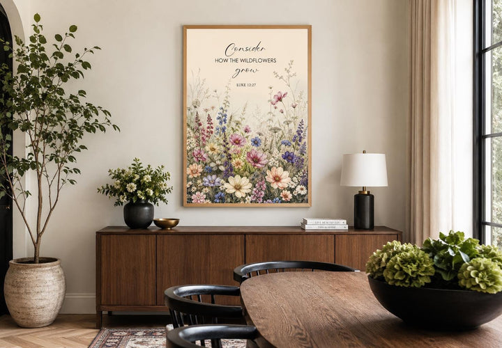Wildflower watercolor art with Luke 12:27 scripture verse in a gold frame above a wooden sideboard.