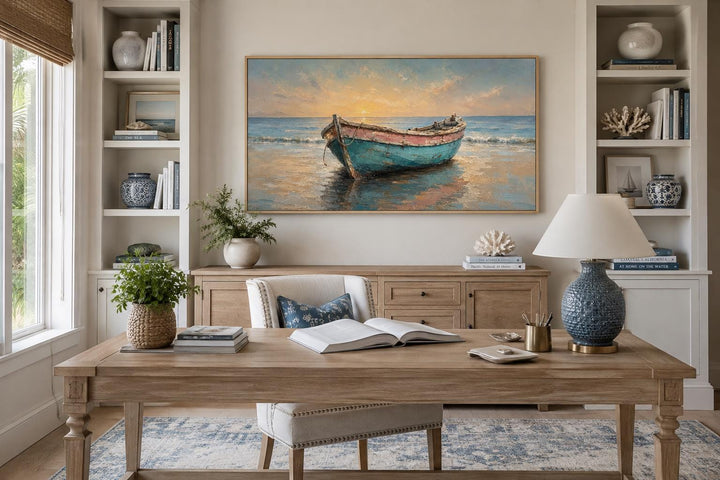 Weathered teal and pink rowboat painting at sunset in a gold frame above a wooden office desk.