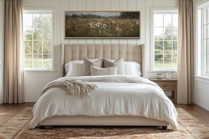 A long horizontal canvas of a muted wildflower field hangs above a bed in a neutral bedroom.