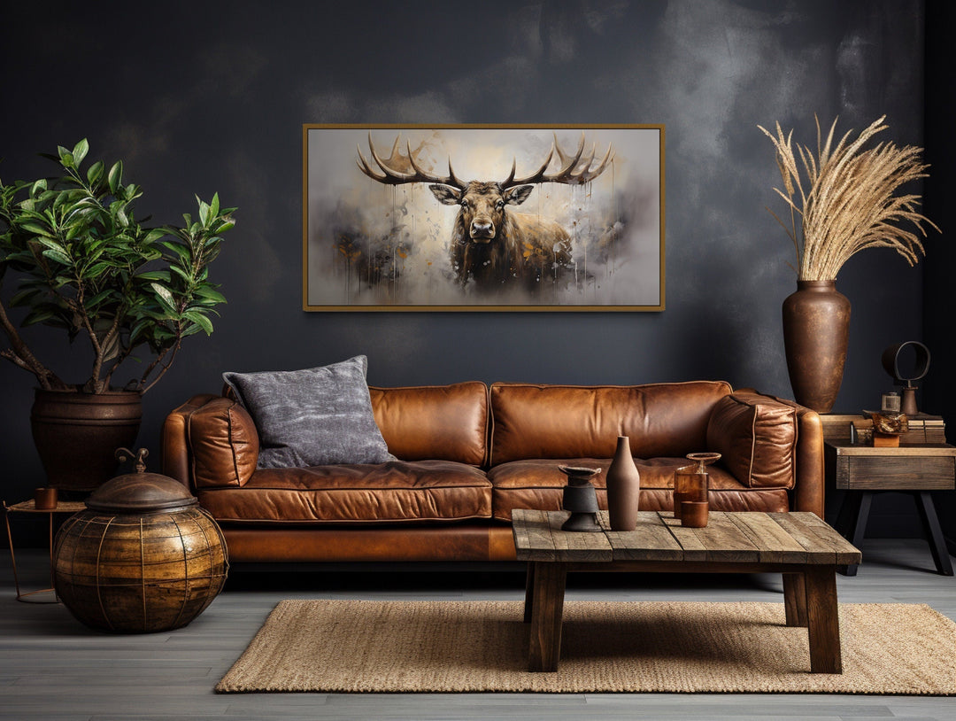 Extra large framed abstract moose canvas print hanging above a brown leather sofa in a rustic room.