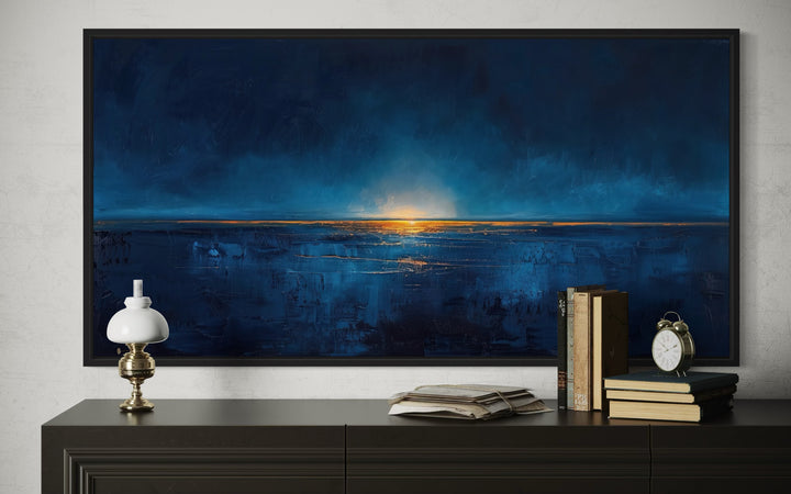 Abstract navy blue and gold ocean painting in a black frame above a dark wood dresser.