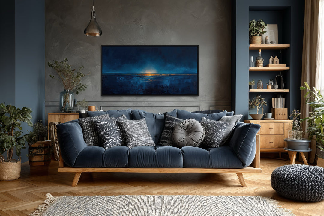Abstract navy blue and gold calm ocean painting in a black frame above a blue sofa in a living room.