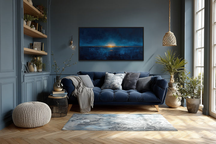 Abstract navy blue and gold ocean painting in a black frame above a blue sofa in a living room.