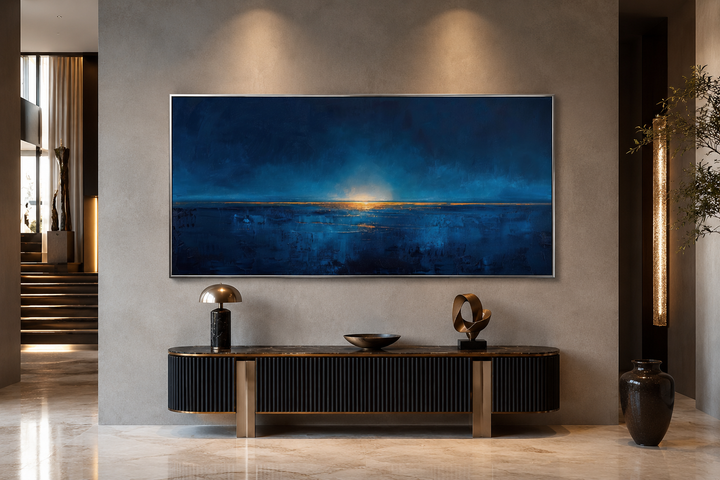 Abstract navy blue and gold ocean horizon painting in a silver frame above a black console table.