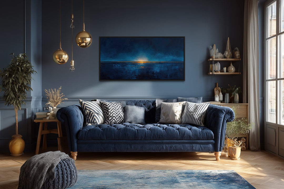 Abstract navy blue and gold ocean painting in a black frame above a blue sofa in a living room.