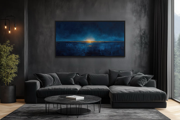 Abstract navy blue and gold ocean painting in a black frame above a dark grey sectional sofa.