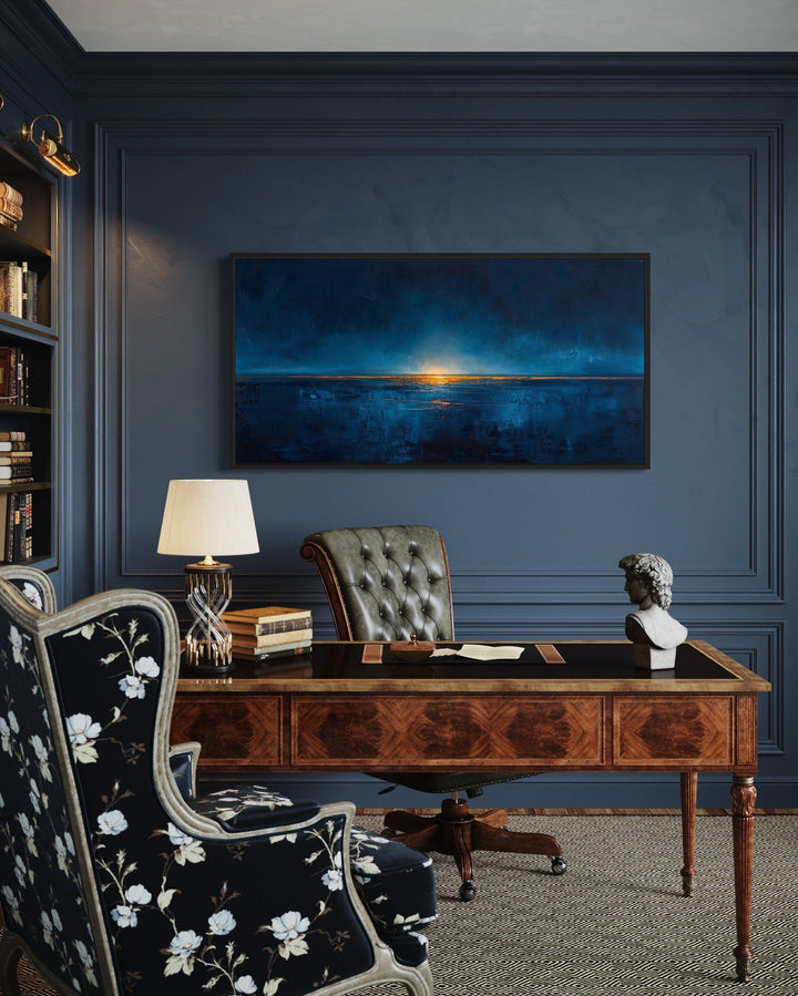 Abstract navy blue and gold ocean painting in a black frame above a classic wooden desk.