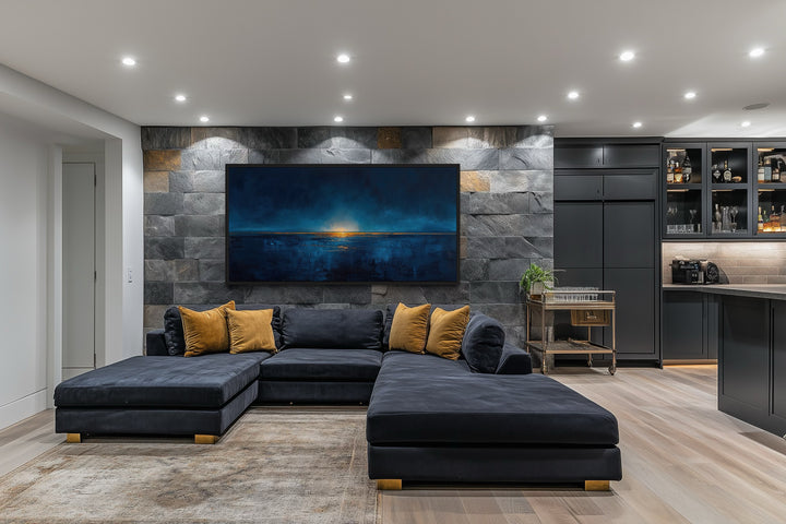 Abstract navy blue and gold ocean painting on a stone wall above a dark blue sectional sofa.